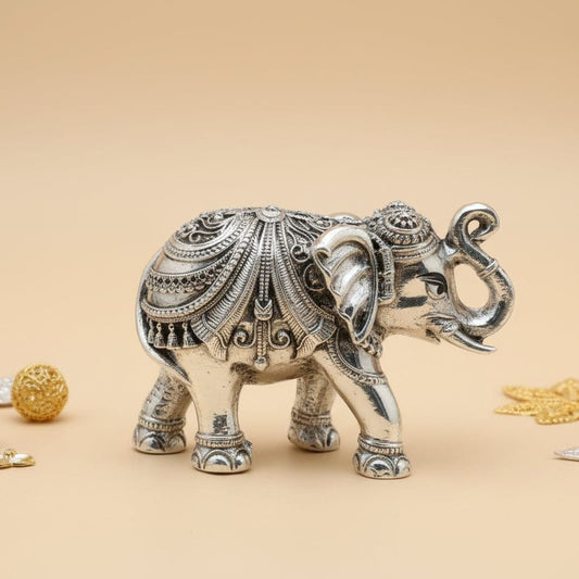 Decorative silver elephant figurine with gold jewelry on a beige background, featuring the brand 'Kanuveeda'.