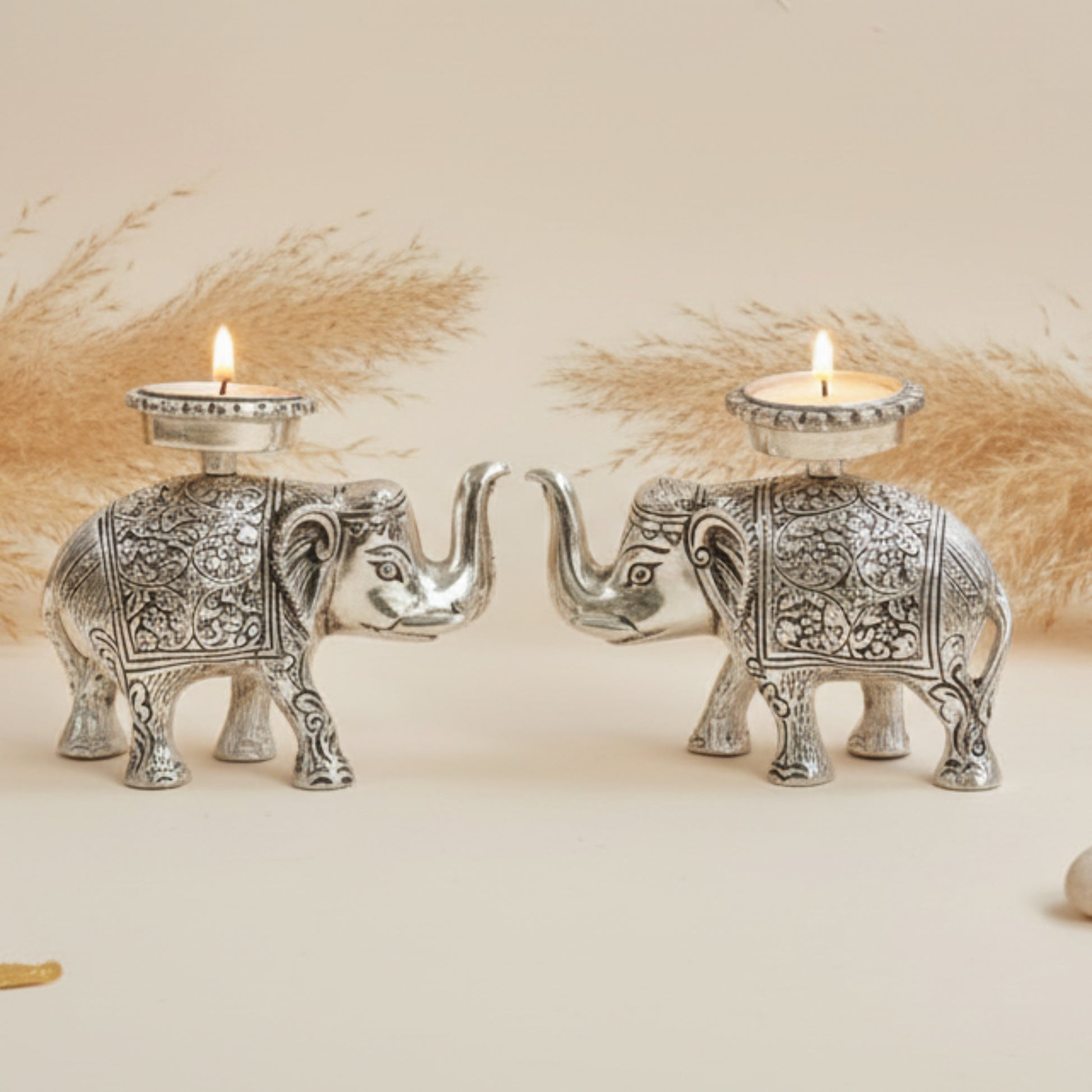 Two silver elephant candle holders on a blue cushion with a plain background